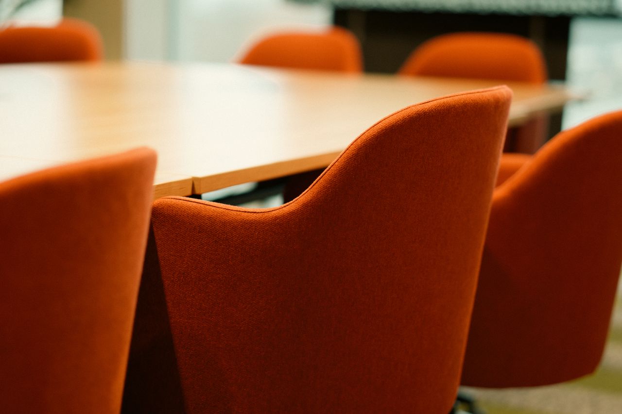 Services Close-up view of modern orange chairs around a conference table in an office setting.